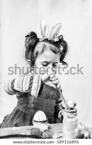 little girl 2 - 4 years in a red dress draws intently the pictures on the eggs with watercolors . at the head of the child ears of a rabbit preparing for Easter . monochrome , black and white