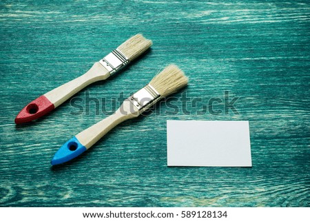 Paint brushes on old wooden background with business card, top view.