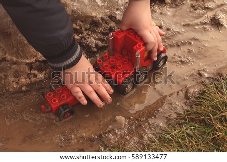 A child playing with a red car in the mud puddle.