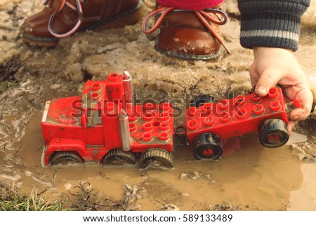A child playing with a red car in the mud puddle.