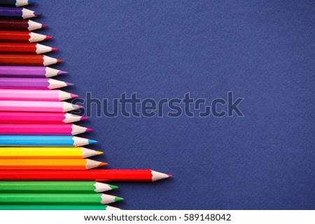 one red pencil standing out from the series of colorful pencils. On blue background.
