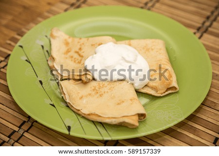 Yellow pancakes with sour cream on a green plate on a brown straw napkin.