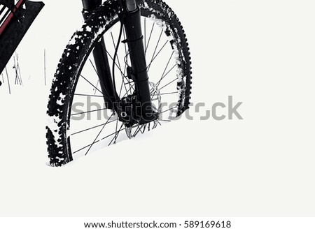 The front wheel of mountain bike stay in powder snow. Lost path under deep snowdrift. Snow flakes melting on dark off road tyre.  Winter weather in the field.