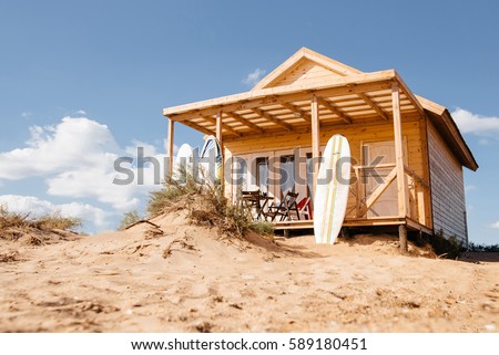 Holiday house on the beach. Wooden house with boards for wind serfing on a sand beach. Summer vacation concept. Royalty-Free Stock Photo #589180451