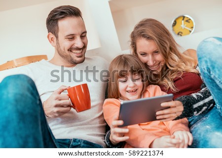 Happy family- mother, father and daughter at home,watching cartoons on a tablet.