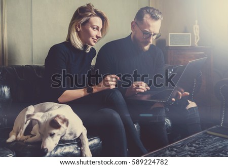Group of young coworkers making great business decisions.People discussing new project at modern meeting room.Man using laptop, woman smiling, white dog sleeping on sofa. Visual effects, flare