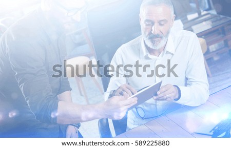Group of two colleagues making great time brake during work process in modern office.Adult bearded man watching digital tablet and smiling.Business people meeting concept.Visual effects