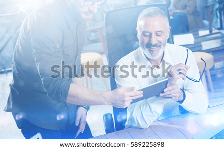 Group of two partners making great idea during work process in modern office.Adult bearded man watching mobile tablet and smiling.Business people meeting concept.Visual effects