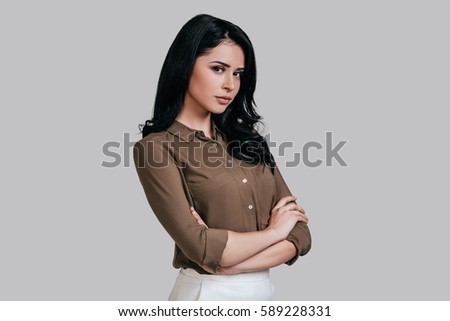 Modern woman. Beautiful young woman in smart casual wear keeping arms crossed and looking at camera while standing against grey background