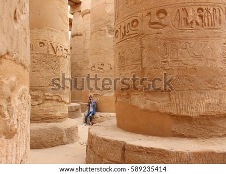Young beautiful woman taking pictures between the columns of the hypostyle hall of Karnak's temple in Luxor, Egypt.