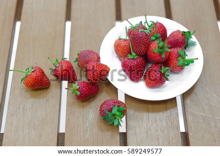 Strawberry 's in a the plate and on the wooden bench.