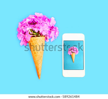 Ice cream cone with flowers and smartphone over blue colorful background top view