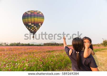 Mother and daughter happy with hot color air balloon over on Beautiful pink cosmos flowers with blue sky