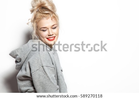 Fashionable smiling woman standing on a white background in a gray sweatshirt with a blank space and looking at the bottom