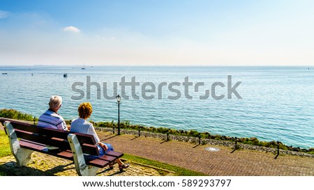 Senior couple enjoying a rest and view of the inland sea named IJselmeer with its wind farms from the historic fishing village of Urk in the Netherlands Royalty-Free Stock Photo #589293797