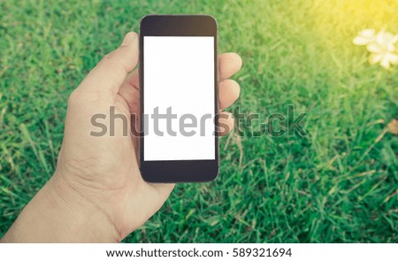 Hand holding smart phone on green grass background.