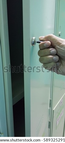 Close up image of a hand hold a key opening a locker.