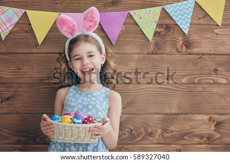 Cute little child wearing bunny ears on Easter day. Girl holding basket with painted eggs. Royalty-Free Stock Photo #589327040