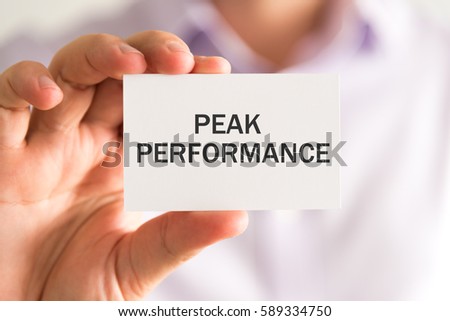 Closeup on businessman holding a card with PEAK PERFORMANCE message, business concept image with soft focus background and vintage tone