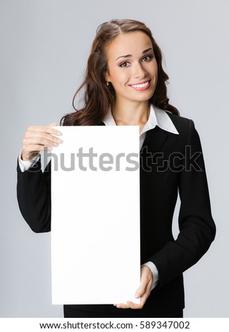 Happy smiling young businesswoman showing blank signboard, over grey background. Business success concept.