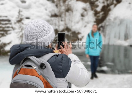 photo on the phone on a journey in the winter. Girl in a hat in a jacket with a backpack Woman photographed blur background water rock ice, missed first trimester waterfall.