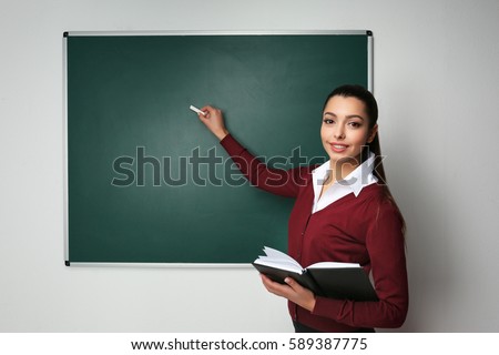 Beautiful young teacher writing on blackboard in classroom