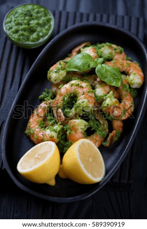 Closeup of tiger shrimps served with chimichurri sauce and lemon in a frying pan