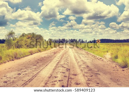 Turn left balck over yellow sign with soil sandy road in countryside. Cinematic road landcape. Argentina. South America