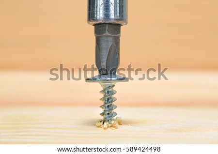Screws screwdriver twist in wooden board. Joinery and construction work close up. Power tool operation. Royalty-Free Stock Photo #589424498
