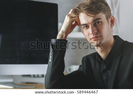 Portrait of handsome caucasian businessman at workplace with empty blurry computer screen. Mock up