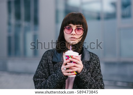 portrait of a young beautiful girl with pink eyes and bright with a cup of coffee in their hands against the backdrop of the city