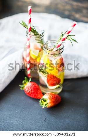 Organic fruit detox drink with lime, strawberry and rosemary herb on rustic background