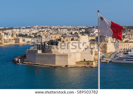 Malta Flag in front of The Ancient limestone walls and towers of Fort St Angelo seen from Upper Barrakka Gardens, view across The Grand Harbour, Valletta, Malta Royalty-Free Stock Photo #589503782
