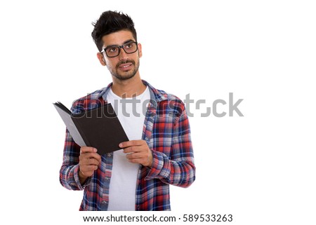 Studio shot of young Persian man wearing eyeglasses and holding book while thinking