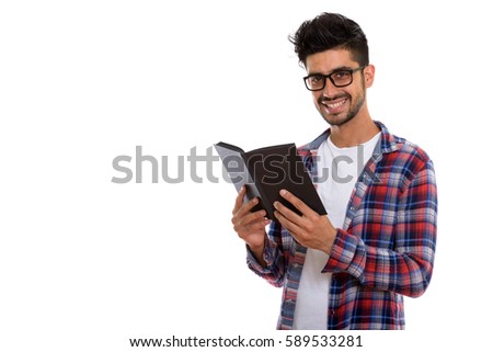 Studio shot of young happy Persian man smiling while wearing eyeglasses and holding book