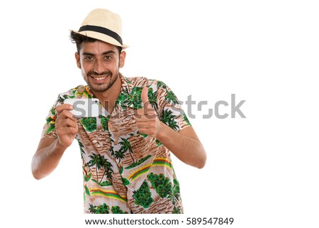 Studio shot of young happy Persian tourist man smiling while taking picture with mobile phone and giving thumb up