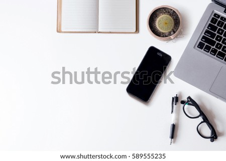 White office desk table with laptop, notebook, smartphone, and cactus. Top view with copy space, flat lay.