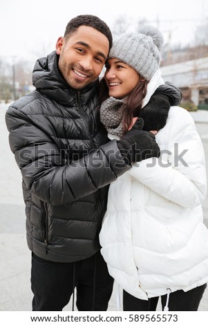 Cheerful multiethnic young couple standing together outdoors in winter