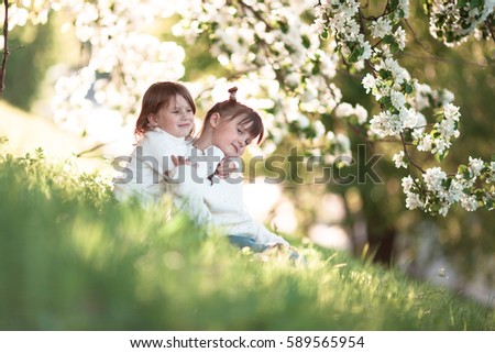 Litte girls/sisters hug around the branches of apple blossom tree, bright, sunny childhood, spring concept, toning lifestyle
