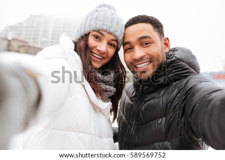 Photo of young happy loving couple skating at ice rink outdoors. Looking at camera and make a selfie.