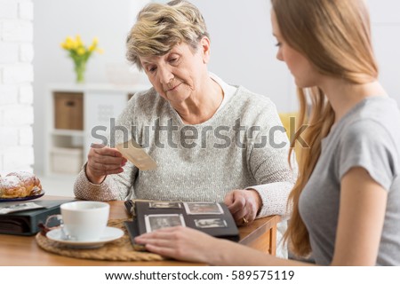 Young woman having coffee and watching old photographs with her grandmother
