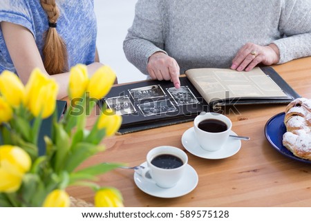 Grandmother having coffee and showing pictures to her granddaughter