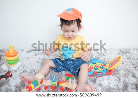 Adorable toddler boy sitting on the carpet and playing colorful toy on a floor