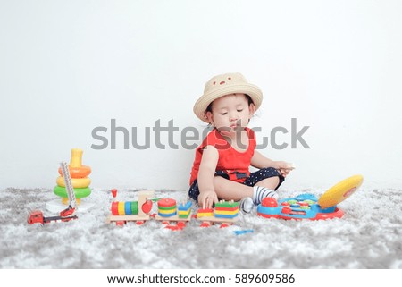 Adorable toddler boy sitting on the carpet and playing colorful toy on a floor