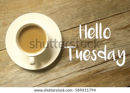 A cup of coffee with HELLO TUESDAY written on a wooden table.
