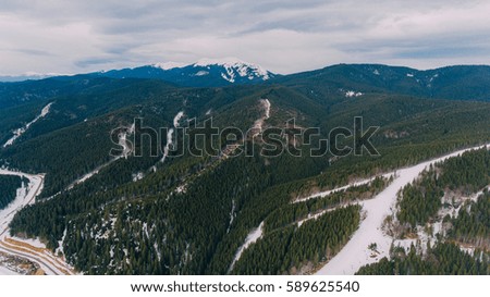 Winter mountains covered with snow around the dense forest and trees. Ski tracks in the snow