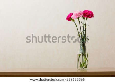 Pink carnation flowers in clear bottle on old wood