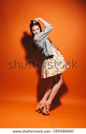 Beautiful teen girl.  orange background. Studio. Model wearing fashionable clothing