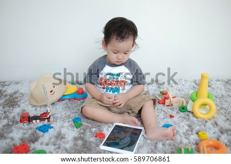Adorable toddler boy sitting on the carpet and playing tablet and colorful toy on a floor