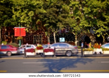 Blurred photo of cars, street, sidewalk and pedestrians background in Shanghai, China. Focus on a couple of China National flags as a street furniture. Urban transportation and green city concept.